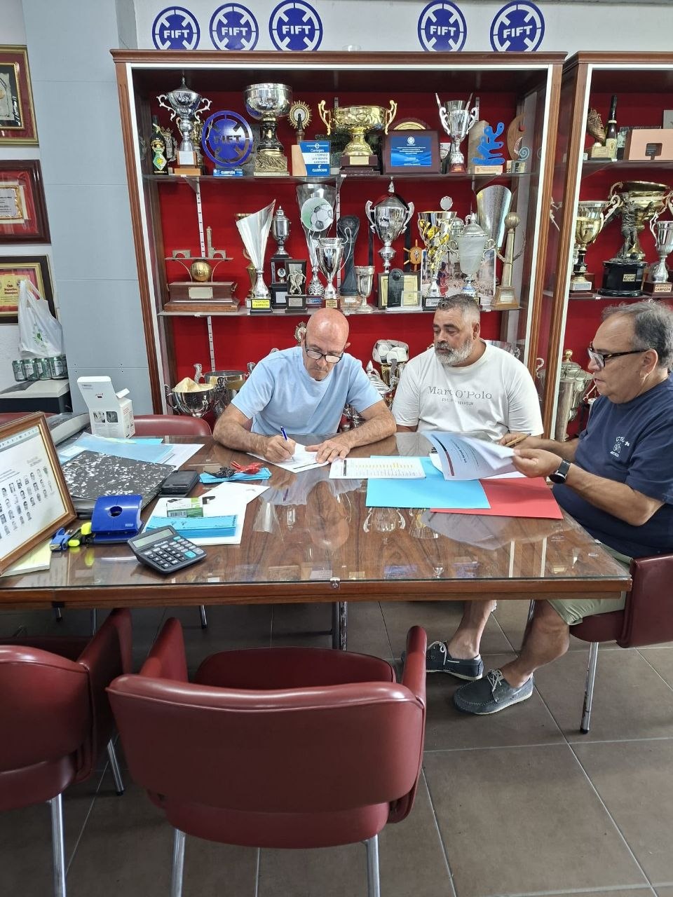 Representantes de los clubes durante la firma del convenio, junto a documentación y trofeos